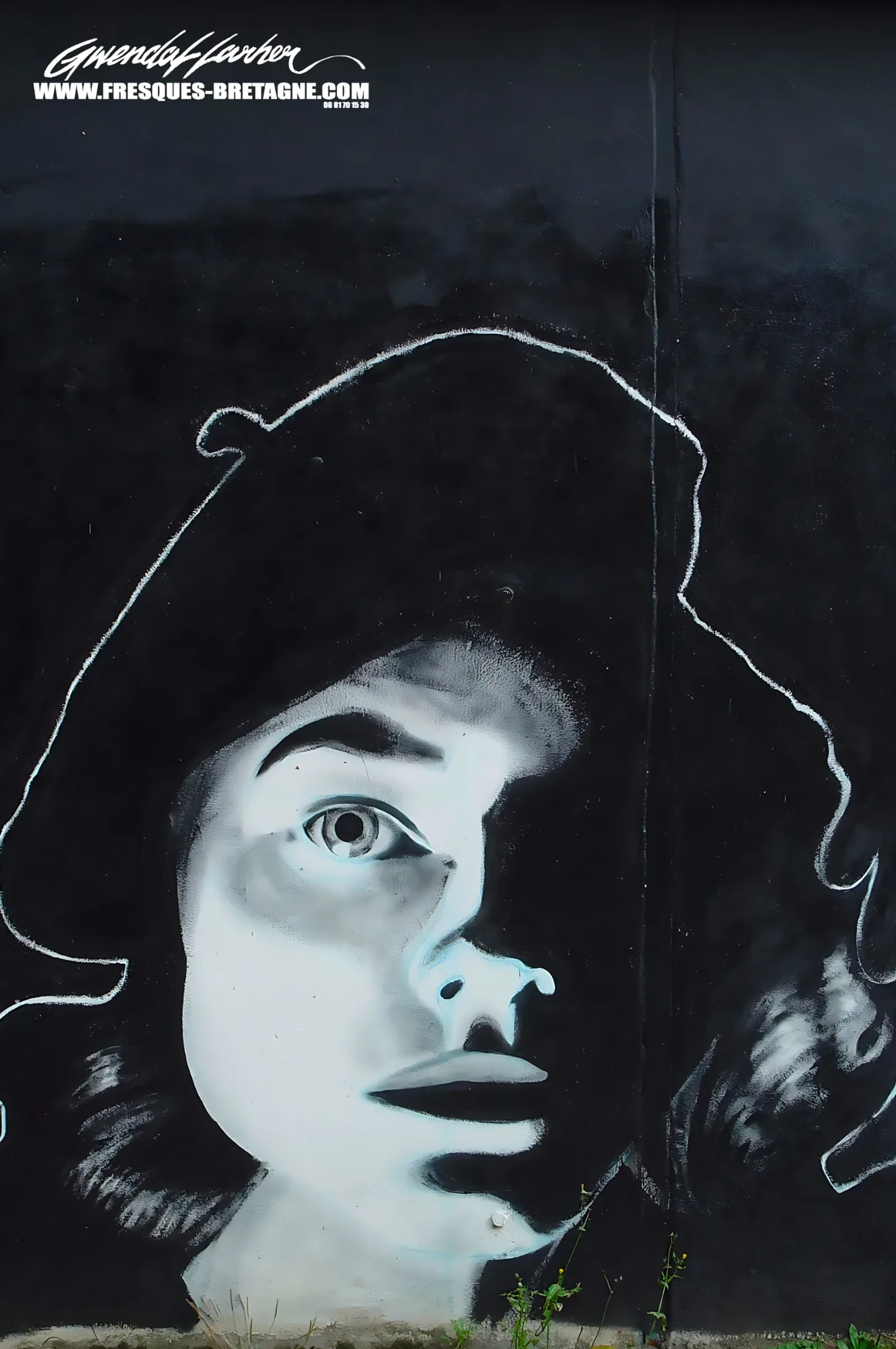 Portrait street art noir et blanc d'une jeune femme au béret, visage éclairé sur mur noir et contour tracé à la craie blanche, fresque murale d'un artiste graffeur